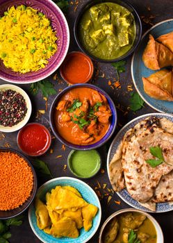 Assorted indian food on dark wooden background. Dishes and appetizers of indian cuisine. Curry, butter chicken, rice, lentils, paneer, samosa, naan, chutney, spices. Bowls and plates with indian food