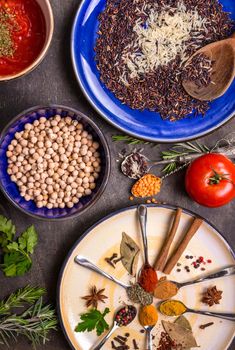 Table served with traditional for asian or eastern cuisine food. Cereal grains, beans, spices on colorful plates. Lentil, basmati and wild rice mix, chick-pea, tomato chutney, pita. Ingredients for indian or eastern food