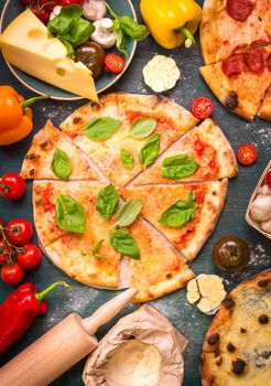 Delicious sliced pizza and ingredients for making pizza. Flour, cheese, tomatoes, basil, pepperoni, mushrooms and rolling pin over wooden background. Top view. Pizza ready to eat