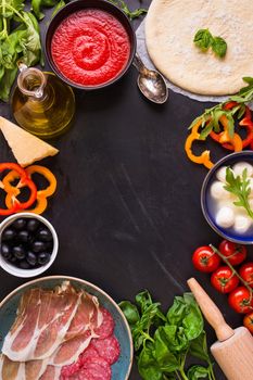 Pizza making background. Ingredients for making pizza. Space for text. Pizza dough, flour, cheese, mozzarella, tomatoes, basil, pepperoni, olives and rolling pin over black chalkboard. Top view