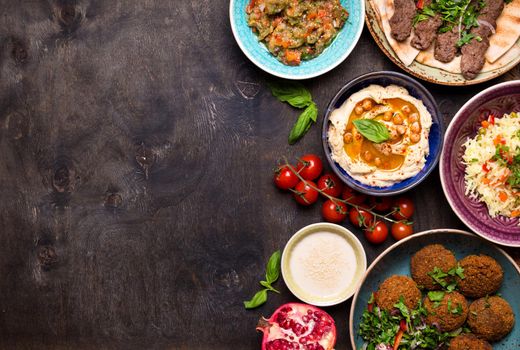 Middle eastern or arabic dishes and assorted meze on a dark background. Meat kebab, falafel, baba ghanoush, hummus, rice with vegetables, tahini, kibbeh, pita. Halal food. Space for text. Top view