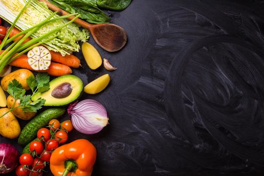 Vegetables, herbs, raw ingredients for cooking and wooden spoon on rustic black chalk board background. Healthy, clean eating concept. Vegan or gluten free diet. Space for text. Top view. Salad making