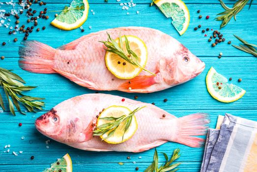 Fresh fish tilapia ready to cook. Raw fish with herbs, lemon, salt, pepper on wooden rustic background. Ingredients for cooking or making healthy dinner. Diet/healthy eating concept. Preparing fish