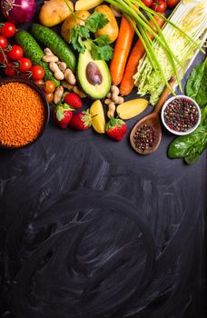 Vegetables, fruits, lentils, raw ingredients for cooking, spoon on rustic black chalk board background. Healthy, clean eating concept. Vegan or gluten free diet. Space for text. Top view. Food frame