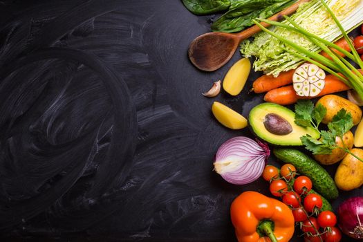 Vegetables, herbs, raw ingredients for cooking and wooden spoon on rustic black chalk board background. Healthy, clean eating concept. Vegan or gluten free diet. Space for text. Top view. Salad making