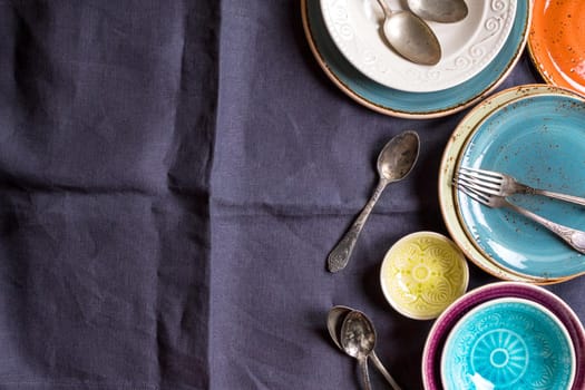 Vintage multicolored empty plates and bowls on a gray linen tablecloth. With antique spoons and forks. Space for text. Table setting. Shabby chic/retro style. Top view. Rustic kitchen. Copy space