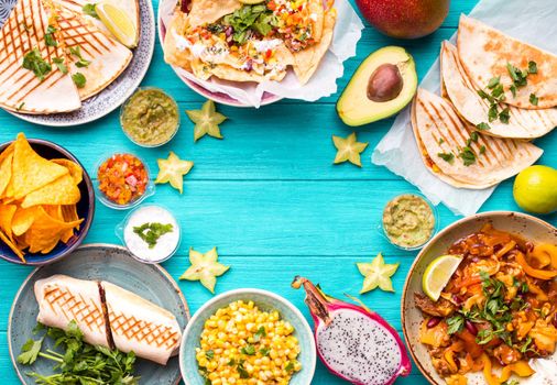 Traditional Mexican food background. Table with different Mexican dishes. Cheese nachos, tacos, guacamole, quesadilla, burrito, fajitas, tortilla chips, Mexican fruits. Tex-Mex cuisine. Space for text