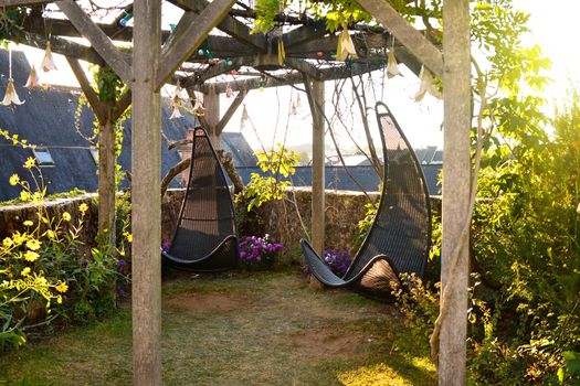 Wicker hanging chairs in the garden with green nature background and sun