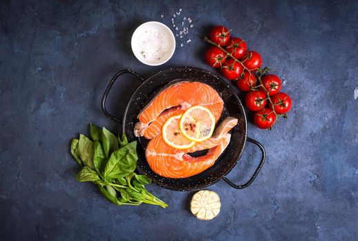 Raw fresh fish with vegetables ready to cook. Raw salmon steaks with lemon, spices and herbs in a pan. Ingredients for cooking on a rustic concrete background. Diet and healthy food. Fish for dinner