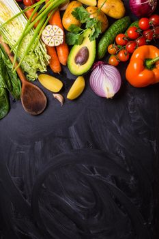 Vegetables, herbs, raw ingredients for cooking and wooden spoon on rustic black chalk board background. Healthy, clean eating concept. Vegan or gluten free diet. Space for text. Top view. Salad making