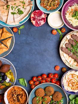 Middle eastern or arabic dishes and assorted meze on concrete rustic background. Meat kebab, falafel, baba ghanoush, hummus, sambusak, rice, tahini, kibbeh, pita. Halal food. Space for text. Top view