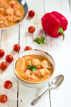 Delicious chicken stew with paprika in a bowl on a white wooden table. With fresh cherry tomatoes, red bell pepper and parsley. Traditional hungarian dish paprikash. Comfort food. Selective focus