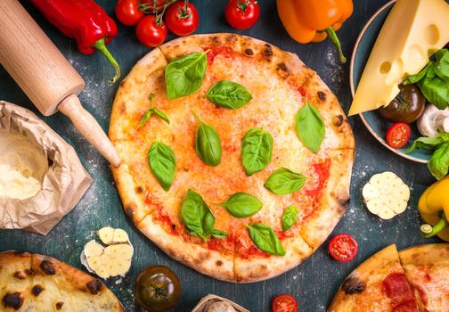 Delicious baked pizza and ingredients for making pizza. Flour, cheese, tomatoes, basil, pepperoni, mushrooms and rolling pin over wooden background. Top view. Pizza ready to eat