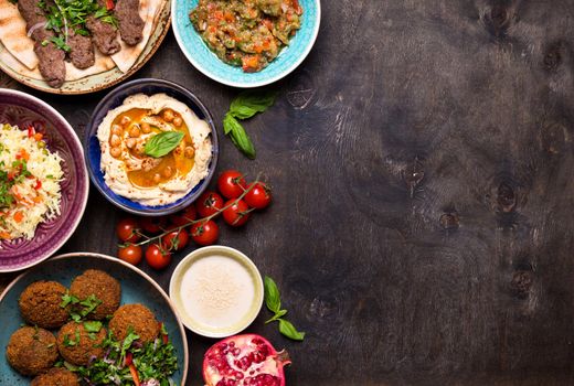 Middle eastern or arabic dishes and assorted meze on a dark background. Meat kebab, falafel, baba ghanoush, hummus, rice with vegetables, tahini, kibbeh, pita. Halal food. Space for text. Top view