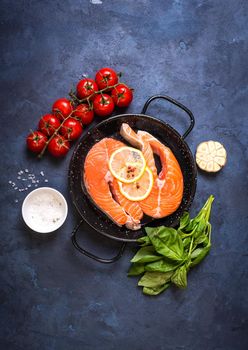 Raw fresh fish with vegetables ready to cook. Raw salmon steaks with lemon, spices and herbs in a pan. Ingredients for cooking on a rustic concrete background. Diet and healthy food. Fish for dinner