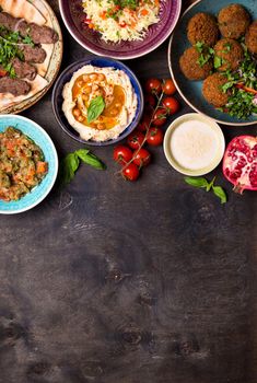 Middle eastern or arabic dishes and assorted meze on a dark background. Meat kebab, falafel, baba ghanoush, hummus, rice with vegetables, tahini, kibbeh, pita. Halal food. Space for text. Top view