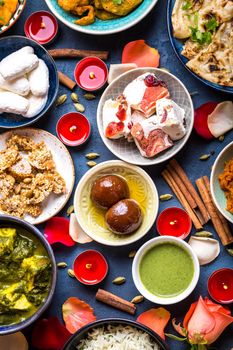 Festive food for Indian festival Diwali. Close-up. Naan, samosa, rice, paneer, sweets. Holiday Indian table with food, sweets, flowers, burning candles. Diwali celebratory dinner. Assorted Indian food