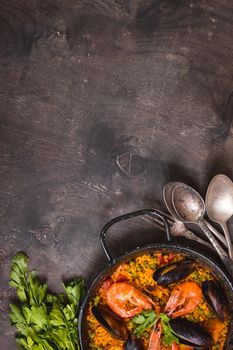 Paella background, space for text. Paella in black pan with saffron rice, peas, shrimps, mussels, squid, meat. Seafood paella, traditional spanish dish. Paella on rustic black wooden table. Top view