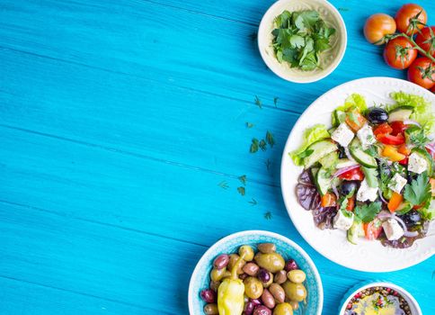 Greek salad background. Bowl with fresh greek salad, tomatoes, olives, olive oil on wooden table. Space for text. Top view. Traditional greek dish. Ingredients for making salad. Mediterranean diet