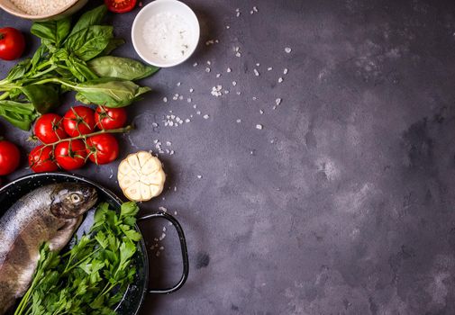 Raw fresh whole fish with vegetables and rice ready to cook. Fresh trout on a pan. Ingredients for cooking on a gray concrete background. Space for text. Diet and healthy food concept. Fish background