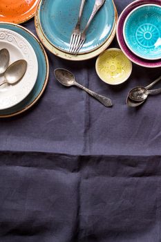 Vintage multicolored empty plates and bowls on a gray linen tablecloth. With antique spoons and forks. Space for text. Table setting. Shabby chic/retro style. Top view. Rustic kitchen. Copy space