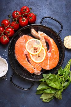 Raw fresh fish with vegetables ready to cook. Raw salmon steaks with lemon, spices and herbs in a pan. Ingredients for cooking on a rustic concrete background. Diet and healthy food. Fish for dinner