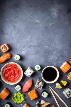 Japanese sushi on a rustic dark background. Sushi rolls, nigiri, maki, pickled ginger, wasabi, soy sauce. Sushi set on a table. Space for text. Top view. Sushi background. Asian or Japanese food frame