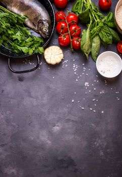 Raw fresh whole fish with vegetables and rice ready to cook. Fresh trout on a pan. Ingredients for cooking on a gray concrete background. Space for text. Diet and healthy food concept. Fish background