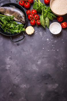 Raw fresh whole fish with vegetables and rice ready to cook. Fresh trout on a pan. Ingredients for cooking on a gray concrete background. Space for text. Diet and healthy food concept. Fish background
