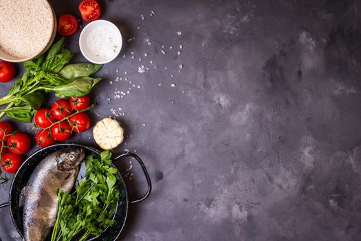 Raw fresh whole fish with vegetables and rice ready to cook. Fresh trout on a pan. Ingredients for cooking on a gray concrete background. Space for text. Diet and healthy food concept. Fish background