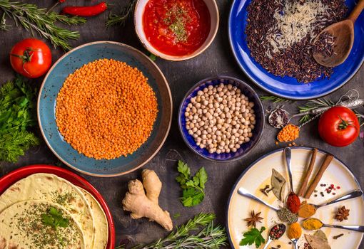 Table served with traditional for asian or eastern cuisine food. Cereal grains, beans, spices on colorful plates. Lentil, basmati and wild rice mix, chick-pea, tomato chutney, pita. Ingredients for indian or eastern food