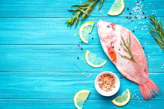 Fresh fish tilapia ready to cook. Raw fish with herbs, lemon, salt, pepper on wooden rustic background. Ingredients for cooking or making healthy dinner. Fish background. Space for text. Diet/healthy