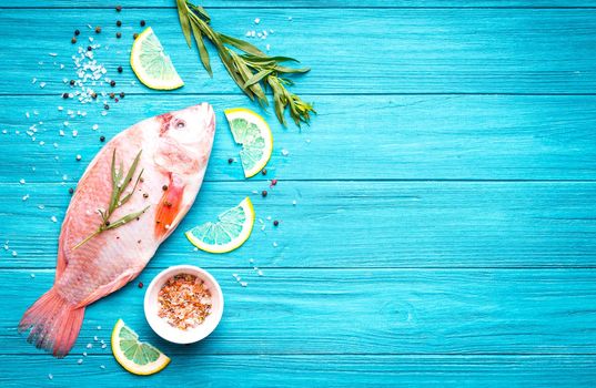 Fresh fish tilapia ready to cook. Raw fish with herbs, lemon, salt, pepper on wooden rustic background. Ingredients for cooking or making healthy dinner. Fish background. Space for text. Diet/healthy