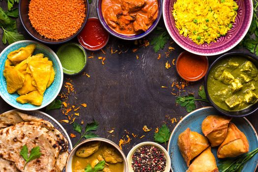 Assorted indian food on dark wooden background. Dishes of indian cuisine. Curry, butter chicken, rice, lentils, paneer, samosa, naan, chutney, spices. Space for text. Bowls and plates with indian food