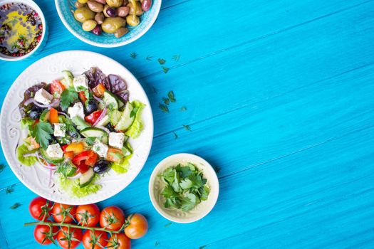 Greek salad background. Bowl with fresh greek salad, tomatoes, olives, olive oil on wooden table. Space for text. Top view. Traditional greek dish. Ingredients for making salad. Mediterranean diet