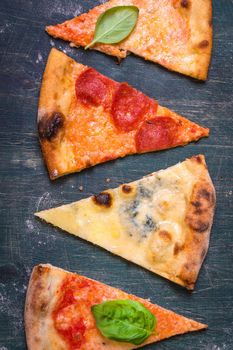 Assorted pizza slices. Margherita, pepperoni, four cheese pizza. Top view. Different types of pizza on the textured old wooden table.