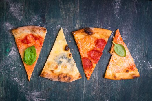 Assorted pizza slices. Margherita, pepperoni, four cheese pizza. Top view. Different types of pizza on the textured old wooden table.