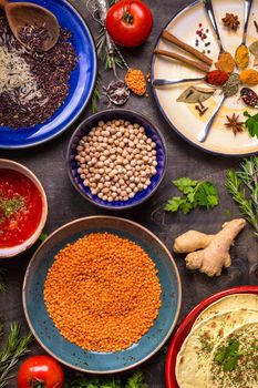 Table served with traditional for asian or eastern cuisine food. Cereal grains, beans, spices on colorful plates. Lentil, basmati and wild rice mix, chick-pea, tomato chutney, pita. Ingredients for indian or eastern food