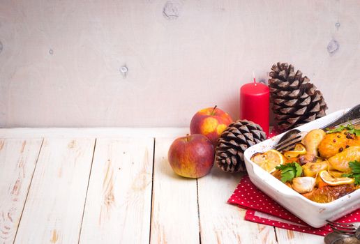 Roasted chicken. Christmas food background. Celebration white wooden table with roasted chicken, apples, decorated with candles, cones, vintage cutlery. Christmas/Thanksgiving dinner. Space for text