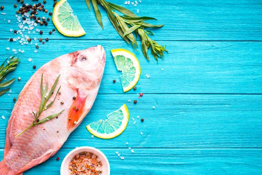 Fresh fish tilapia ready to cook. Raw fish with herbs, lemon, salt, pepper on wooden rustic background. Ingredients for cooking or making healthy dinner. Fish background. Space for text. Diet/healthy