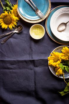 Vintage multicolored empty plates and bowls on a dark gray linen tablecloth with sunflower. With antique spoons and forks. Space for text. Table setting. Shabby chic/retro style. Top view. Copy space