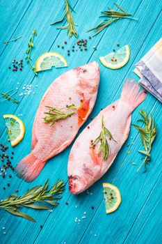 Fresh fish tilapia ready to cook. Raw fish with herbs, lemon, salt, pepper on wooden rustic background. Ingredients for cooking or making healthy dinner. Diet/healthy eating concept. Preparing fish