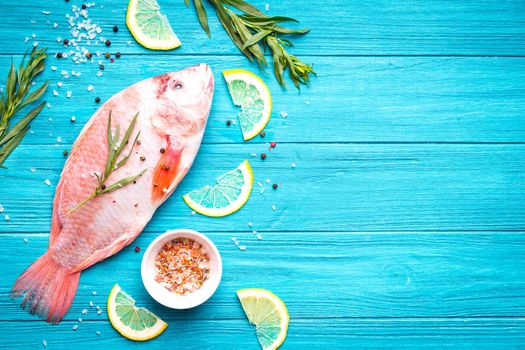 Fresh fish tilapia ready to cook. Raw fish with herbs, lemon, salt, pepper on wooden rustic background. Ingredients for cooking or making healthy dinner. Fish background. Space for text. Diet/healthy