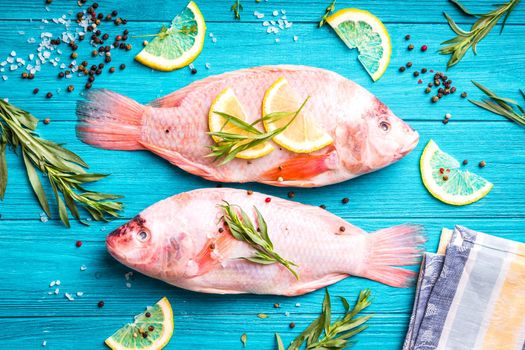 Fresh fish tilapia ready to cook. Raw fish with herbs, lemon, salt, pepper on wooden rustic background. Ingredients for cooking or making healthy dinner. Diet/healthy eating concept. Preparing fish
