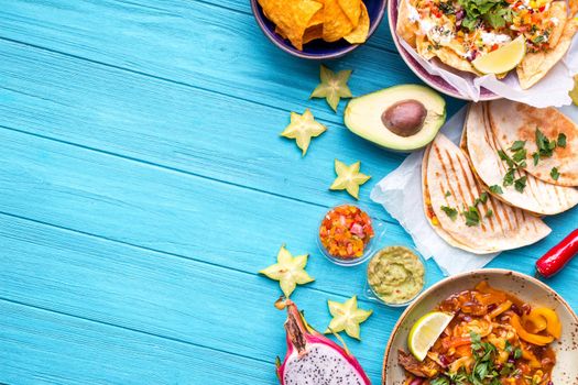 Traditional Mexican food background. Table with different Mexican dishes. Cheese nachos, tacos, guacamole, fajitas, tortilla chips, Mexican fruits. Tex-Mex cuisine. Space for text. Mexico/Texas style