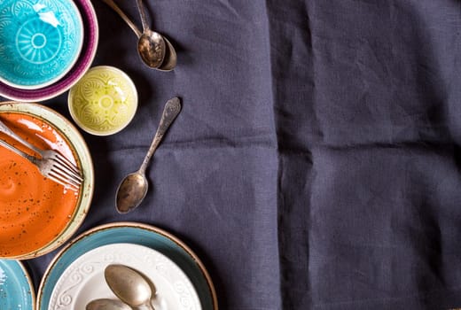 Vintage multicolored empty plates and bowls on a gray linen tablecloth. With antique spoons and forks. Space for text. Table setting. Shabby chic/retro style. Top view. Rustic kitchen. Copy space