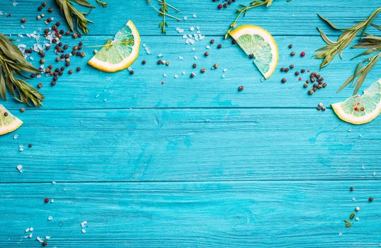 Food seasoning background. Blue coloured rustic wooden background, lemon slices, herbs, pepper, sea salt. Preparing a dinner. Space for text. Close-up. Vivid food frame. Top view. Cooking ingredients