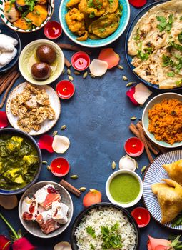 Festive food for Indian festival Diwali. Naan, samosa, rice, paneer, sweets. Background. Holiday Indian table with food, sweets, flowers, burning candles. Diwali celebratory dinner. Space for text.