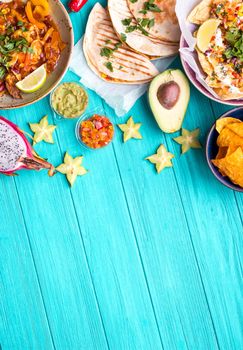 Traditional Mexican food background. Table with different Mexican dishes. Cheese nachos, tacos, guacamole, fajitas, tortilla chips, Mexican fruits. Tex-Mex cuisine. Space for text. Mexico/Texas style