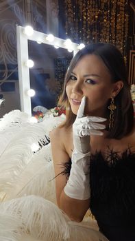 Beautiful asian young woman and decorative ostrich feathers on a gold table next to a make-up mirror. Get ready for the getsby party
